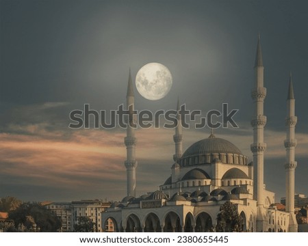 Mosque view. The full moon shines over the mosque in the early morning twilight. Text on the Building: English Translation: Quran verse