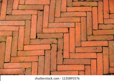 Mossy Diagonal Pattern Of Brick Pavement In A Herringbone Style For Background, Old Orange Bricks Tiled Floor With Zigzag Pattern. Old Peeling Chevron Zigzag Diagonal Brickwork Texture Background.