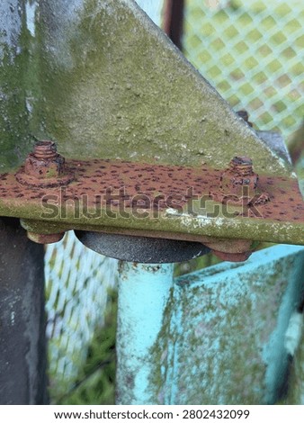 Mossy rusty metal bracket with corroded bolts on weathered blue paint