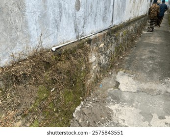 A mossy stone wall runs alongside a building exterior creating a rustic scene Perfect for architectural or nature photography