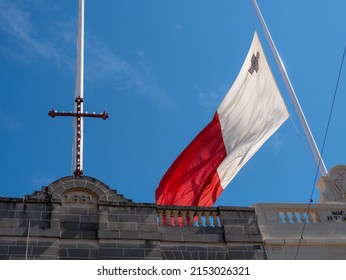 Mosta, Malta, 15 Apr 2022: Maltese Flag Waving Next To A Cross