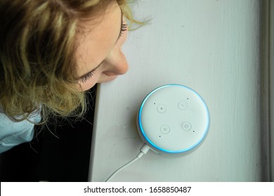MOSTERTON ENGLAND FEBRUARY 2020 - Teenage girl talking to an Amazon Alexa Echo Dot. Girl smiling talking to an Amazon Alexa
