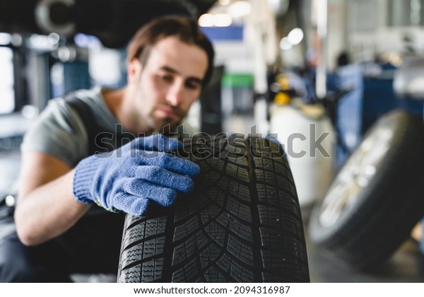 MOT. Vehicle inspection. Caucasian male young car\
technician mechanic changing repairing fixing wheel tire of\
automobile at service\
station
