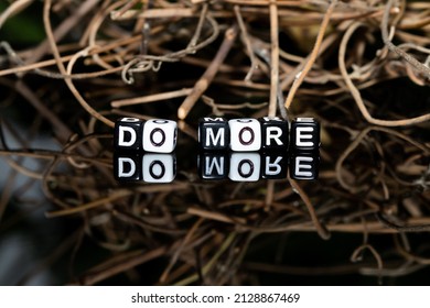 Mote alphabet blocks arranged into "do more" against a background of dry twigs of vines.