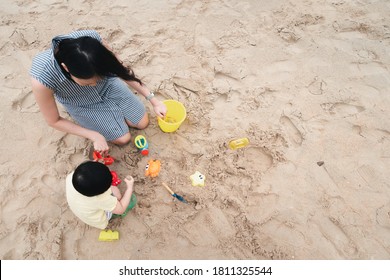 Mother And 3 Years Old Asian Kid Play Sand On The Beach. Background For Family Life And Education. Holiday With Children.