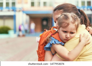 Mother Accompanies The Child To School. Mom Supports And Motivates The Student. The Little Girl Does Not Want To Leave Her Mother. Fears Primary School. Communication Problems. Attachment To Parents.