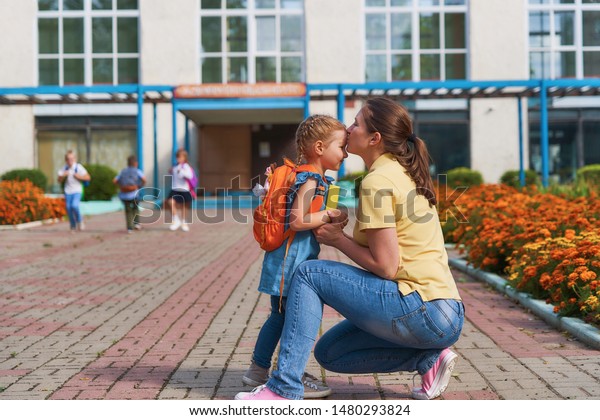 mother accompanies the child to school. mom\
supports and motivates the student.caring mother gently kisses her\
daughter on the forehead. positive little girl fun going to primary\
school.back to school