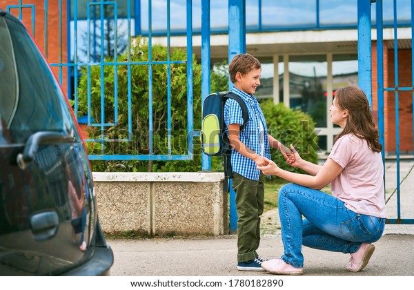 mother accompanies the child to school. mom\
encourages the student to accompany him to school.caring mother\
looks tenderly at her son going to school.mother to son before\
entering school near the\
car