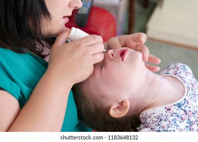 Mother administering medication eye drops to young daughter at home	 - Powered by Shutterstock