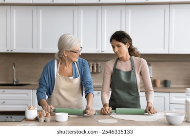 Mother and adult daughter talking while rolling out dough for pastries, standing together in modern domestic kitchen, wear aprons, cooking, lead conversation, sharing news, engage in culinary at home - Powered by Shutterstock