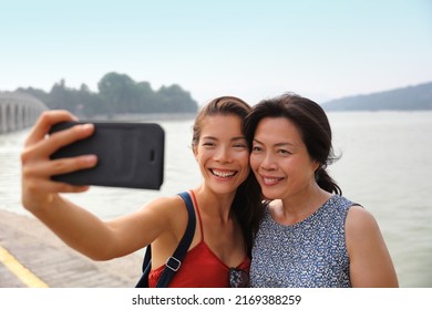 Mother adult daughter traveling together in Asian taking selfie picture with mobile phone. Smiling Asian family outside