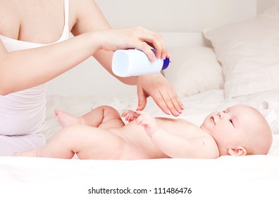 Mother Applying Baby Powder Before Putting Diapers On Her Four Month Old Baby In Bed At Home