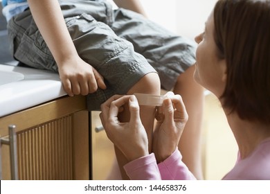 Mother Applying Bandage On Her Son's Knee At Home