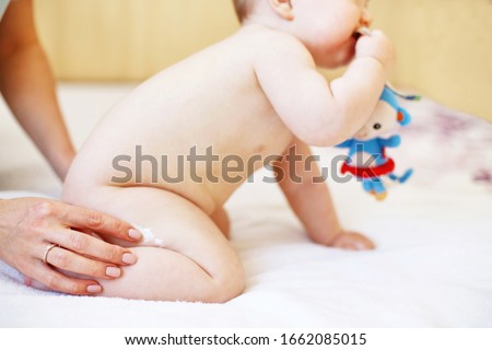 mother applying some cream by her hand to the baby ass for skin care. baby skin care with cream