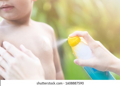 Mother Applying Sun Screen Spray On Her Baby Boy In At The Sea Beach For Swim.Mom And Kids Use Spray For Protection Sun On Body.Spraying Insect Repellent On Skin Outdoor.