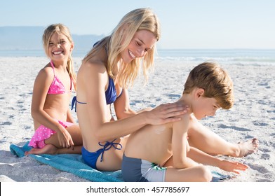 Mother Applying Sunscreen Lotion On Son Back At Beach. Mother Preparing Children For Bath In Sea. Happy Family At Beach Applying Sun Protection.
