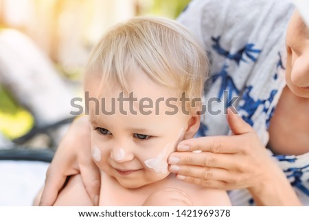 Mother applying sunscreen protection creme on cute little toddler boy face. Mom using sunblocking lotion to protect baby from sun during summer sea vacation. Children healthcare at travel time