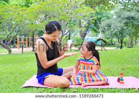 Mother appying body lotion for daughter's in the summer park.