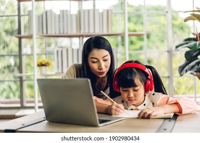 Mother And Asian Kid Little Girl Learning And Looking At Laptop Computer Making Homework Studying Knowledge With Online Education E-learning System.children Video Conference With Teacher Tutor At Home