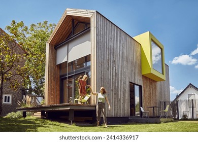 Mother assisting daughter in jumping outside tiny house at yard - Powered by Shutterstock