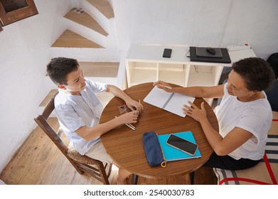 A mother assists her son with homework at the dining table. The sunlit room creates a warm, focused setting, highlighting the bond and cooperation in a bright educational atmosphere. - Powered by Shutterstock