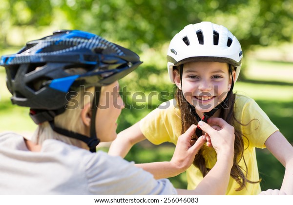 Mother attaching her daughters cycling helmet on a\
sunny day