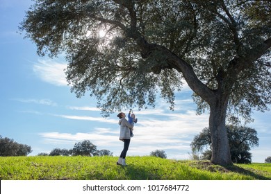 Mother And Baby Boy Playing Under Acorn Tree. Enjoying Nature In Family Concept