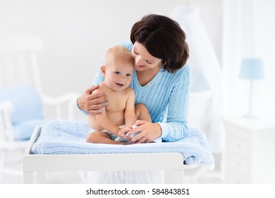 Mother and baby change diaper after bath in white nursery with bed and rocking chair. Little boy on changing table in clean dry nappy. Mom taking care of infant child. Kids room interior and hygiene. - Shutterstock ID 584843851