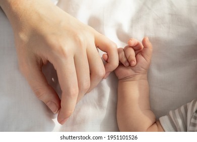 Mother Baby Connection. Newborn child holding his mom's hand while they lying in bed, touching mum's arm with his tiny fingers, top view, cropped image, closeup - Shutterstock ID 1951101526