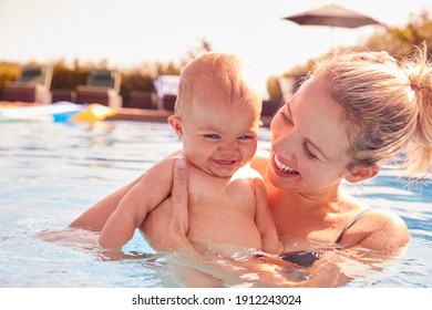 Mother With Baby Daughter Having Fun On Summer Vacation Splashing In Outdoor Swimming Pool