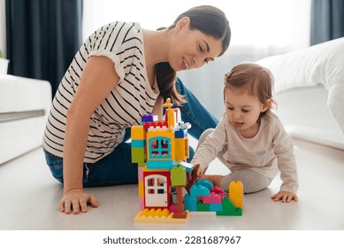 Mother and baby daughter playing with toys on bedroom floor - Powered by Shutterstock