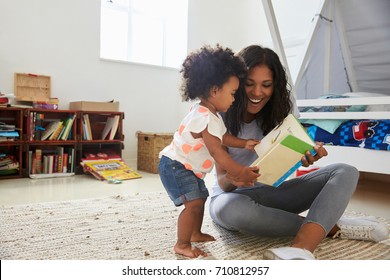 Mother And Baby Daughter Reading Book In Playroom Together