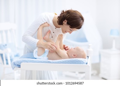 Mother and baby in diaper on changing table. Mom changing nappy on baby boy. Kids nursery. Infant hygiene and care products. Diapers for young children. Mother playing with child in white bedroom.