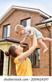 Mother And Baby In Front Of The House. Family Portrait Outside New Home.