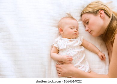 Mother and baby girl lying in bed and sleeping with the mother holding her baby