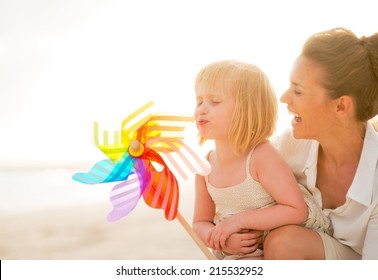 Mother and baby girl playing with colorful windmill toy on the beach in the evening - Powered by Shutterstock