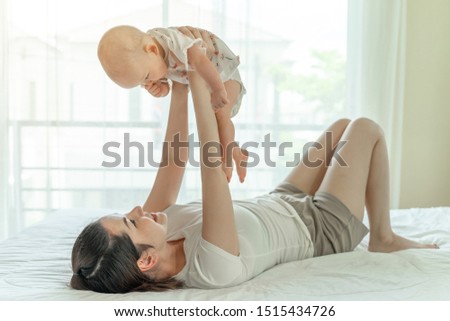Mother and baby happily tease each other on a white bed - mom and baby concept