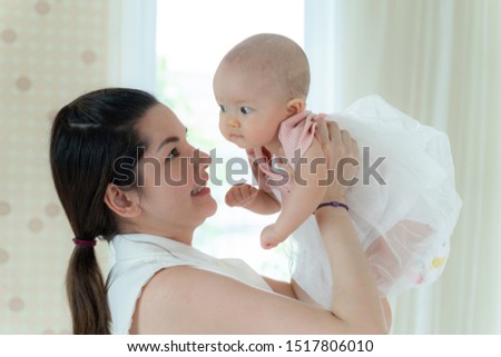 Mother and baby happily tease each other on a white bed - mom and baby concept