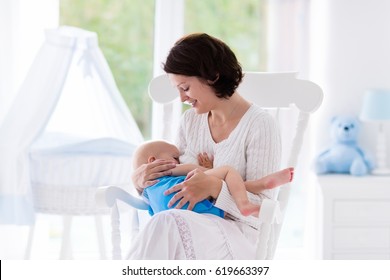 Mother and baby at home. Breastfeeding and healthy infant nutrition. Young woman nursing her newborn child sitting in white rocking chair in sunny nursery with crib and window. Parent and kid at home