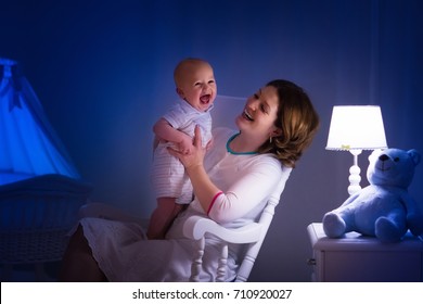 Mother And Baby Reading A Book In Dark Bedroom. Mom And Child Read Books Before Bed Time. Family In The Evening. Kids Room Interior With Night Lamp And Bassinet. Parent Holding Infant Next To Crib.