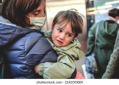 Mother and baby run away from the war. Ukrainian war refugees shelter and help center, little boy cry on her mother's shoulder. Face is in protect mask . - Shutterstock ID 2142293005