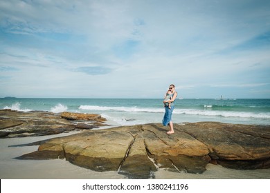 mother with baby stay on beach this rock in Thailand. baby sleep on hand. on background sea and blue sky