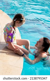 mother with baby in swimming pool. a young woman with her daughter persuades teach to swim. family fun by the pool