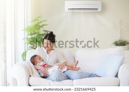 Mother and baby under cool air conditioner. Comfortable temperature at family home. Cooling and heating device. Asian mom and kid on couch under cold breeze. Air conditioning on hot summer day.
