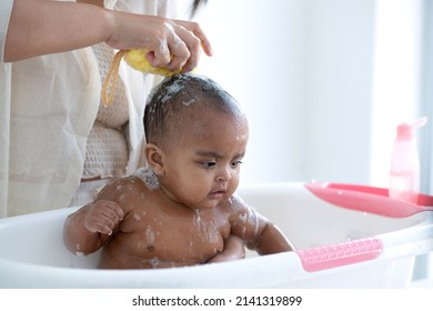 Mother Bathing Her African Baby In The Bathtub At Home, Mom Cleaning Her Baby Hair With Shampoo And Sponge, Baby Care Concept