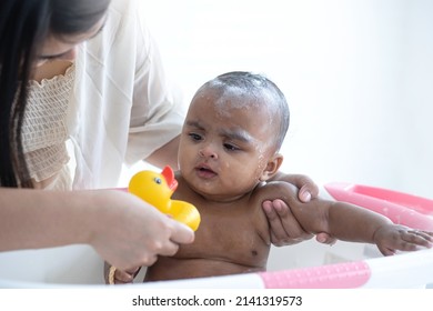 Mother Bathing Her African Little Baby In The Bathtub At Home, Baby Looking Yellow Duckling, Baby Care Concept