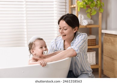 Mother bathing her cute little baby in tub at home - Powered by Shutterstock