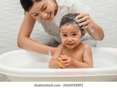 mother bathing and washing her infant baby hair with shampoo while playing a rubber duck toy in a bathtub  - Powered by Shutterstock