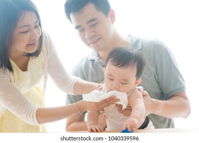 Mother blow baby nose with tissue paper. Asian family spending quality time at home, living lifestyle indoors.