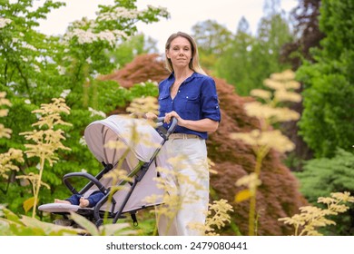 A mother in a blue shirt and white pants walks through a lush park pushing a stroller with her baby. - Powered by Shutterstock